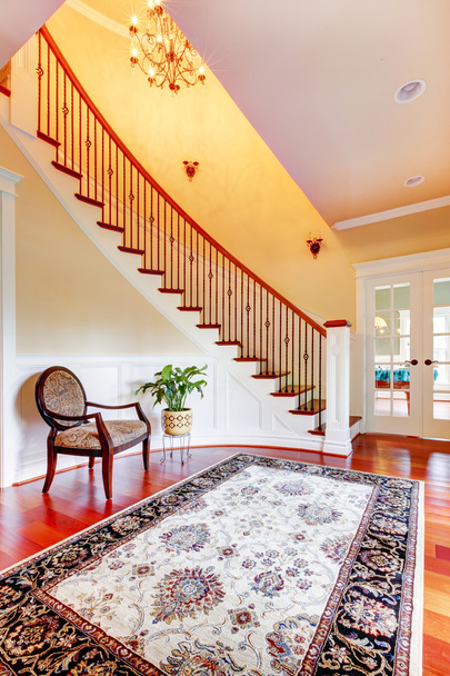 Entrance with curved staircase and luxury rug with chair. - Foto, Imagen