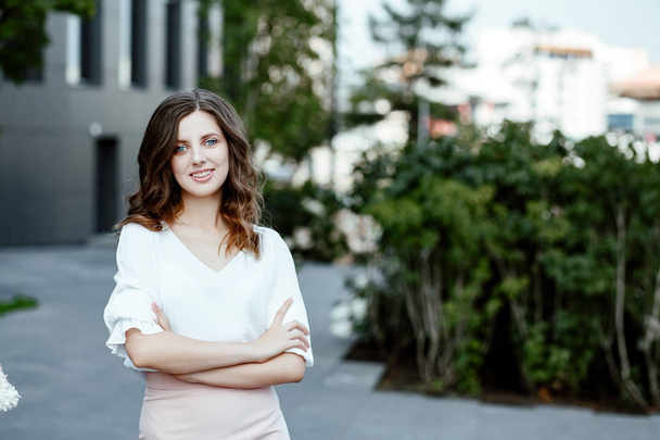 Office style. A business portrait of the young woman in a white blouse and a pink skirt against the background of city architecture. - Fotografie, Obrázek
