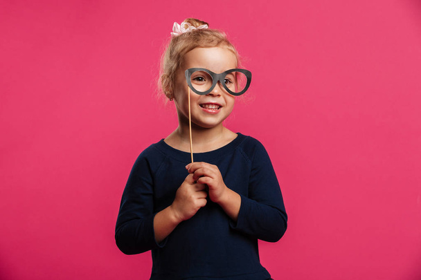Smiling young girl using paper eyeglasses and looking at camera - Photo, image