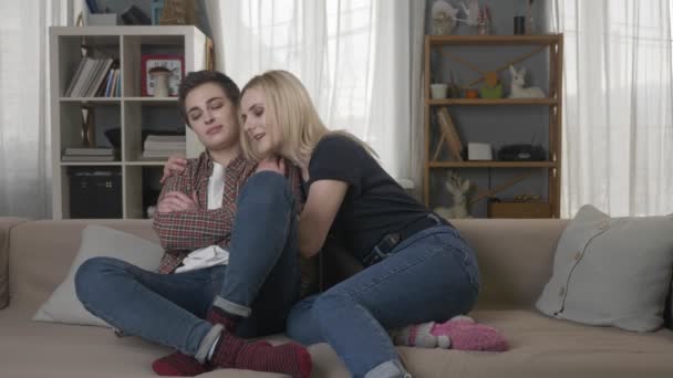 Δύο νέοι λεσβίες κορίτσια κάθονται στον καναπέ, ένα κορίτσι με ξανθά μαλλιά που αγκαλιάζει τον σύντροφό της. 60 fps - Πλάνα, βίντεο