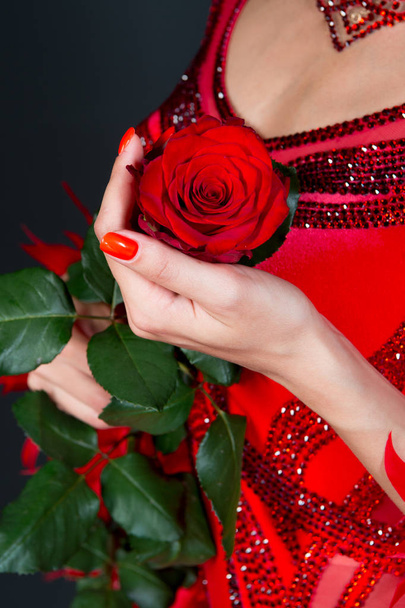 Love, desire, passion. Rose flower in female hand in red dress on dark background. Valentine present, gift, surprise. Valentines day, birthday, holiday celebration. - Zdjęcie, obraz