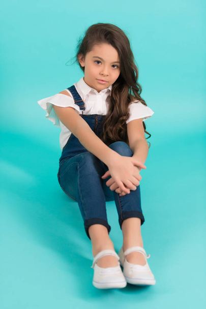 Small child with long brunette hair in jeans overall on blue background. Fashion, style concept. Beauty, look, hairstyle. Childhood, preteen, youth, punchy pastel - Photo, Image