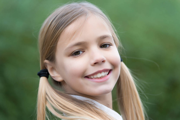 Little girl smile on natural background, childhood. Child with blond hair ponytails smiling outdoor. Happy childhood concept. Beauty, look, hairstyle. - Photo, Image