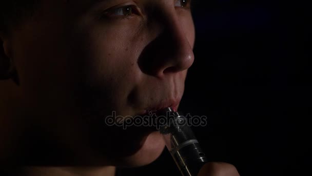 Man smoking electronic cigarette vapor on black background - Filmati, video