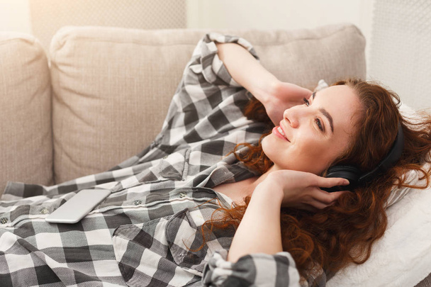 Young woman in headphones on beige couch - Fotoğraf, Görsel