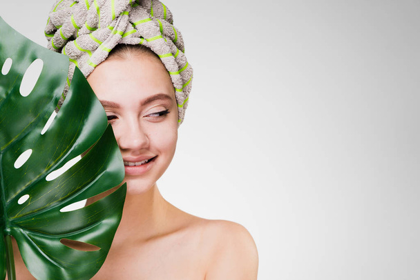 woman with a towel on her head holds a large leaf - Φωτογραφία, εικόνα