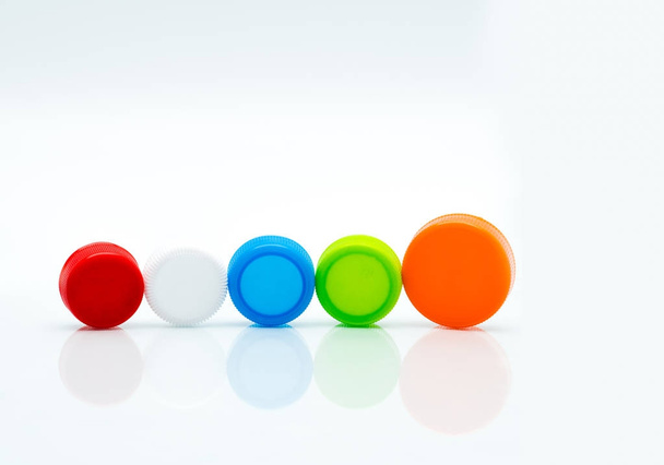 Différentes tailles de bouchons à vis en plastique ronds de couleur blanche, verte, rouge, bleue et orange dans une ligne sur fond blanc et espace de copie
. - Photo, image