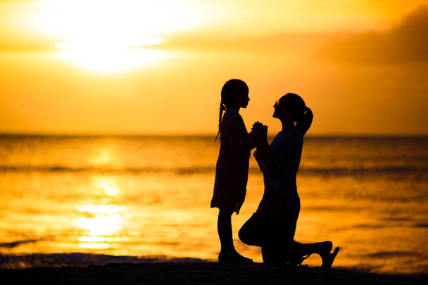 Niña y silueta madre feliz en la puesta de sol en la playa
 - Foto, Imagen