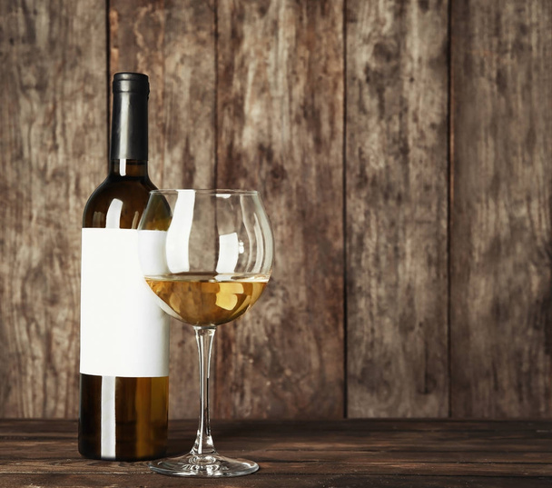 Glass of white wine and bottle with blank label on wooden table. Mock up for design - Fotoğraf, Görsel