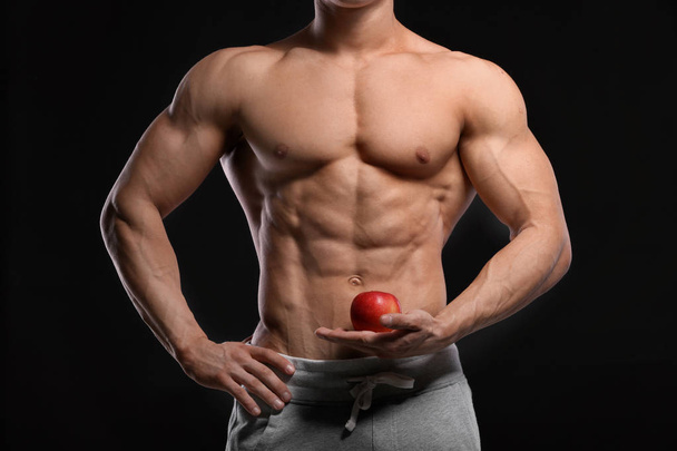 Handsome muscular young man with apple on black wall - Zdjęcie, obraz