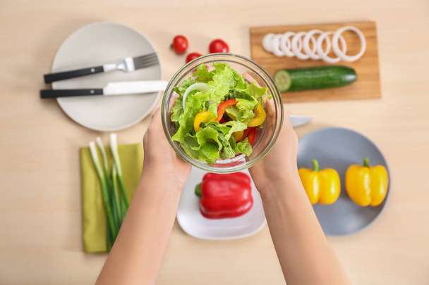 Mujer sosteniendo tazón de sabrosa ensalada de verduras sobre la mesa con ingredientes
 - Foto, imagen