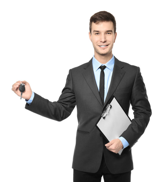 Handsome car salesman with key and clipboard on white background - Foto, Imagen