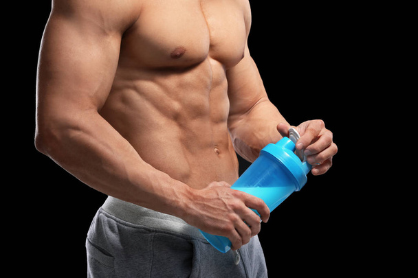Handsome muscular young man with protein shake on black wall - Foto, afbeelding