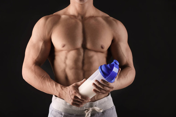 Handsome muscular young man with protein shake on black wall - Φωτογραφία, εικόνα
