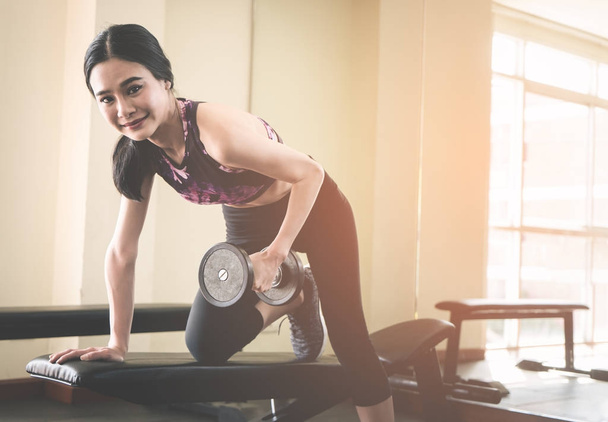 Slim asian woman is lifting weight dumbbell in fitness gym - Photo, Image