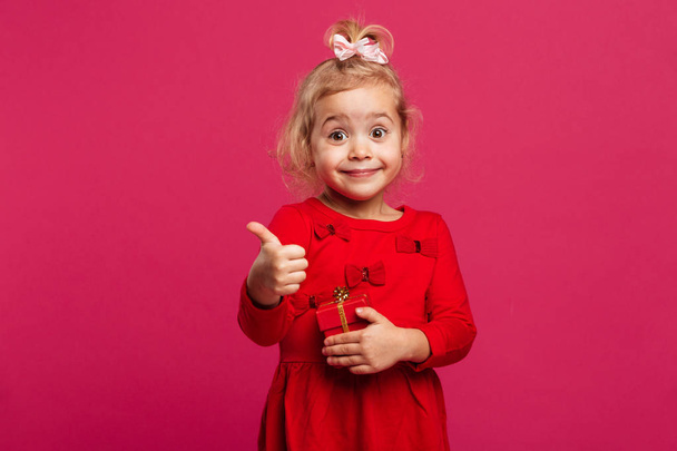 Happy young blonde girl in red dress showing thumb up - Foto, Imagen