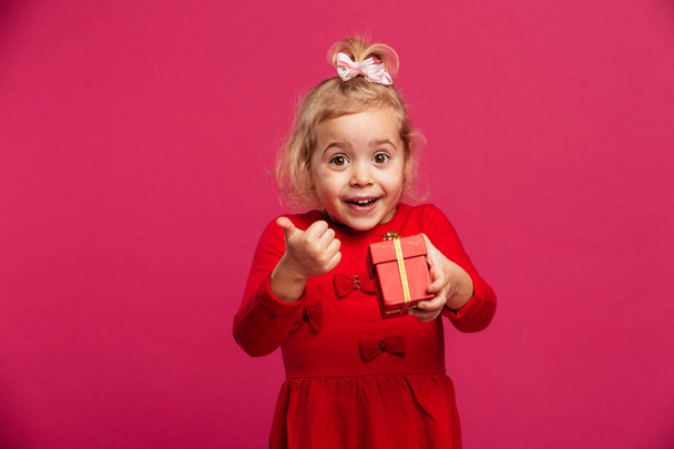 Cheerful young blonde girl in red dress holding gift box - Foto, Imagen