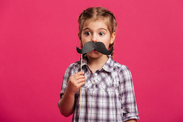 Shocked little girl child holding fake moustache. - Foto, afbeelding