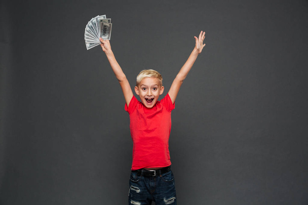 Picture of screaming surprised little boy child standing isolated over grey background. Looking camera showing money. - Фото, зображення