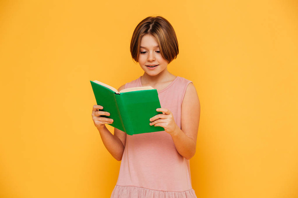 Cheerful girl reading book isolated over yellow - Valokuva, kuva
