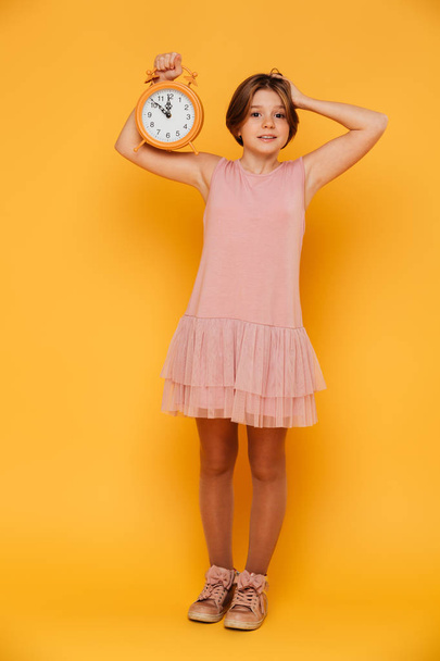 Surprised smiling girl showing alarm clock and holding her head isolated - Photo, image