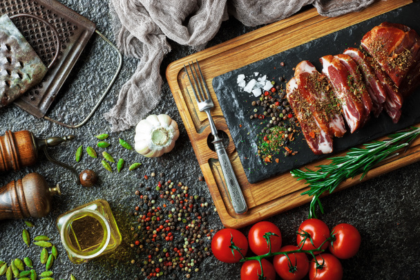 Сырое мясо на кухонном столе на металлическом фоне в композиции с кухонными принадлежностями
 - Фото, изображение