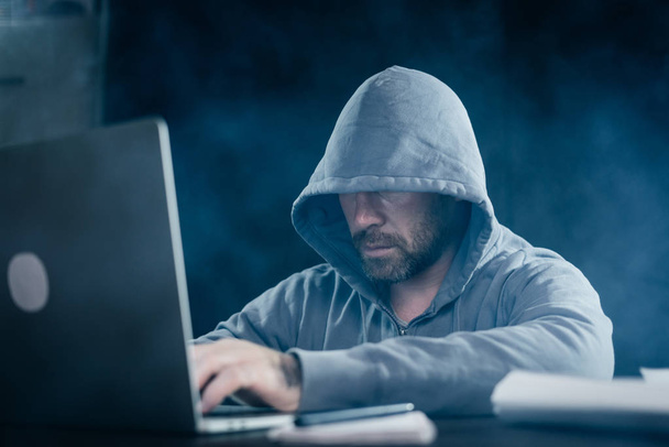 guy hacker sitting in a dark room behind a laptop - Фото, изображение