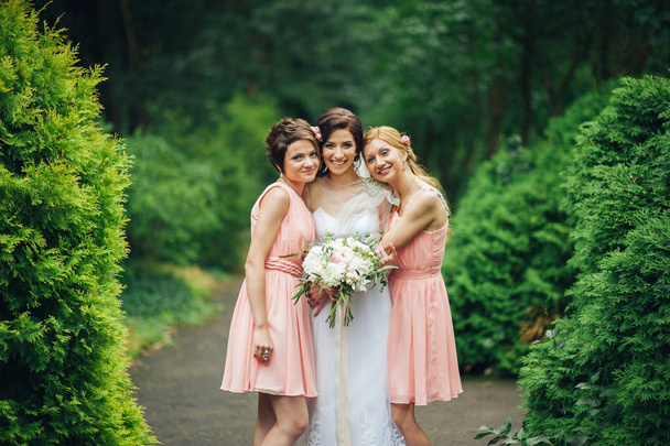 young happy bride with bridesmaids in park on wedding day - Zdjęcie, obraz