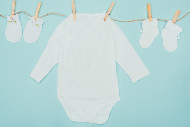 Draufsicht auf Baby-Bodys und Socken, die auf Seilen trocknen, isoliert auf blau - Foto, Bild