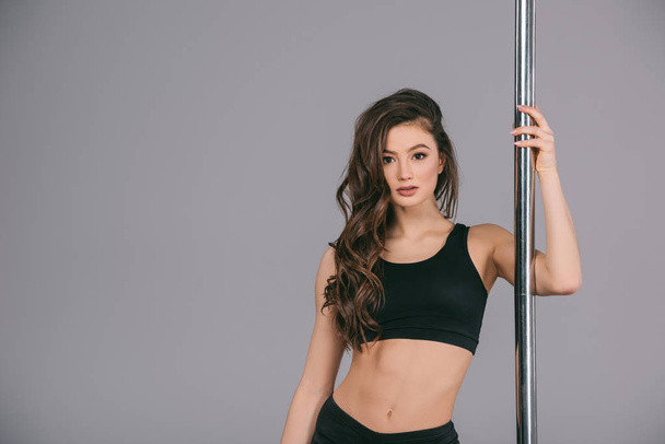 beautiful sporty young woman standing near pole and looking at camera on grey  - Photo, Image