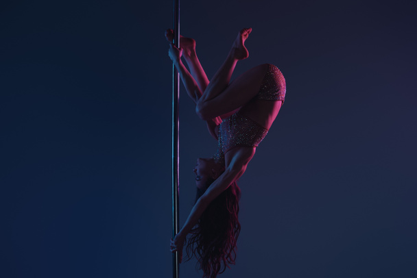 вверх ногами спортивной молодой женщины, танцующей с шестом на синем
 - Фото, изображение