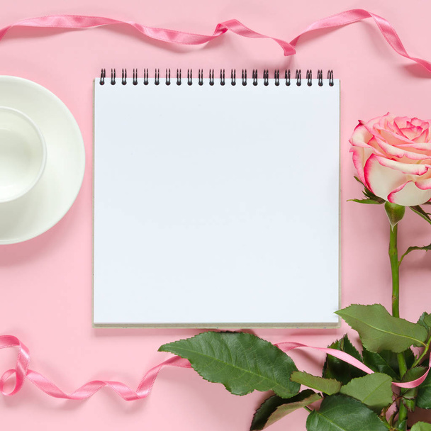 Pink blooming fresh rose flower with cup for coffee and notebook on pink background - Zdjęcie, obraz