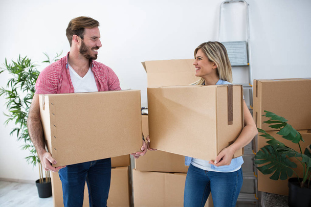 Smiling young couple holding boxes and packing for moving - Foto, Imagem