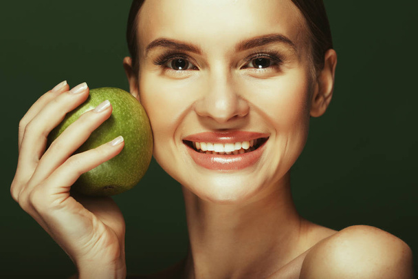 Head shot of woman holding green apple against green background - Foto, Imagen
