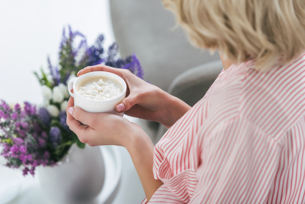 cropped view of blonde woman holding cup of cappuccino with marshmallow - Foto, Bild