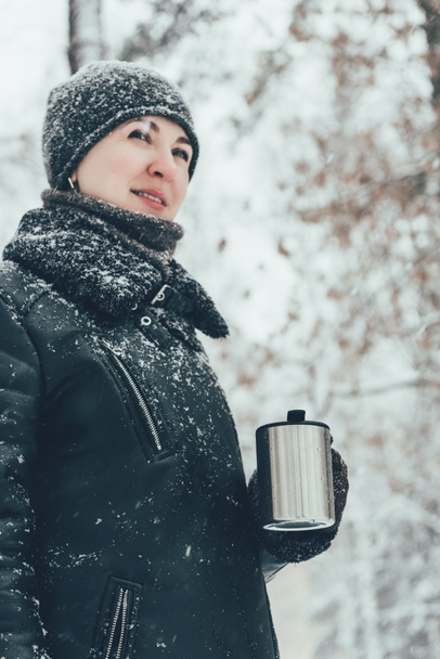 Porträt einer lächelnden Frau mit Thermobecher mit Heißgetränk, die im Winter auf der Straße wegschaut - Foto, Bild
