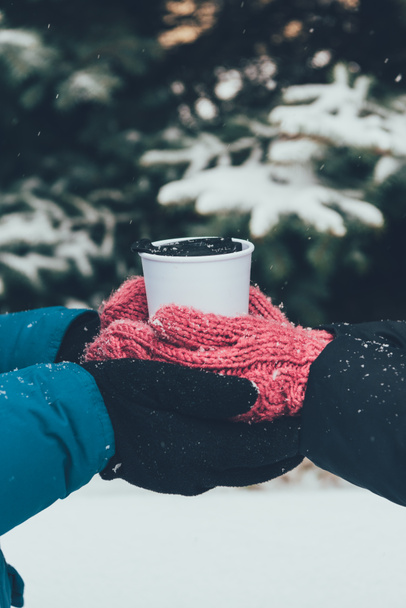 vista parcial de la pareja sosteniendo la termocopa con bebida caliente juntos en el bosque de invierno
 - Foto, imagen