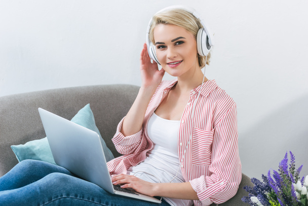 beautiful blonde girl listening music with headphones and using laptop - Foto, Imagem