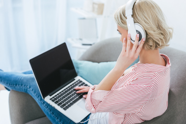 woman listening music with headphones and using laptop with blank screen - Photo, Image