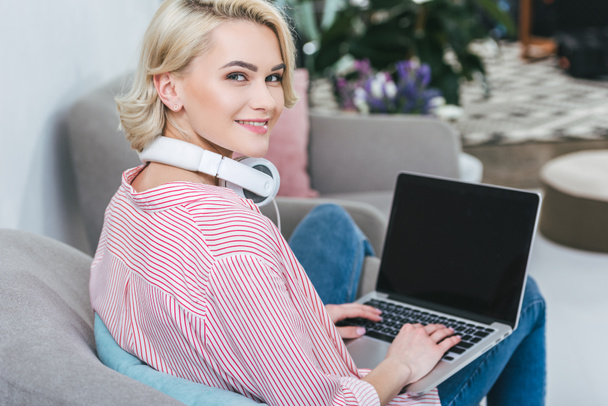 smiling girl listening music with headphones and using laptop at home - Photo, Image