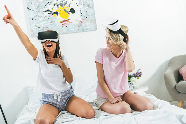 excited girls gesturing and using virtual reality headsets at home - Foto, afbeelding