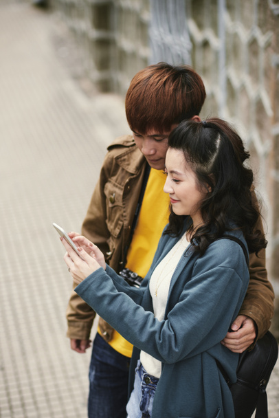 Объятия азиатской молодой пары, читающей сообщение на смартфоне
 - Фото, изображение