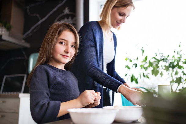 A small girl with her mother cooking at home. - Foto, Bild