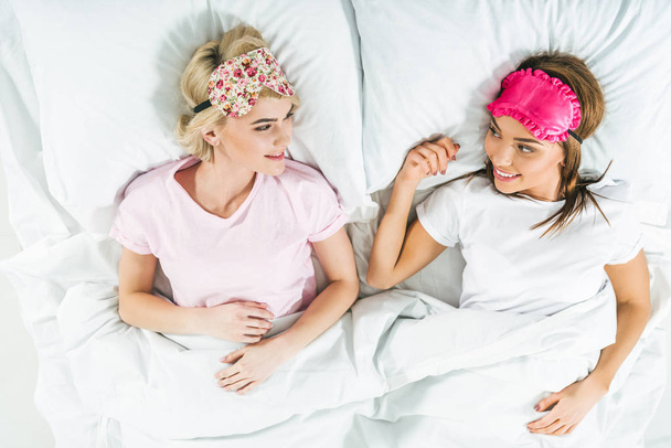 top view of smiling girls in sleeping masks lying on bed - Photo, image