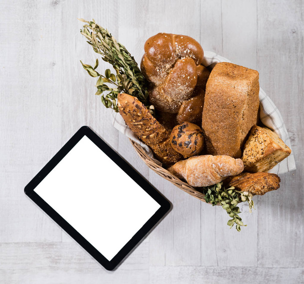 Košík s čerstvým domácím chlebem a digitální tablet na bílém stole  - Fotografie, Obrázek