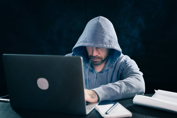 a man hacker is sitting in a room for a laptop smoking and something prints - Photo, Image