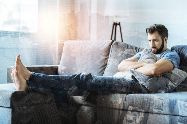 Sad thoughtful man lying on the sofa and looking aside. - 写真・画像