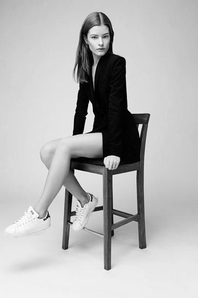 Attractive fashion model sitting on bar stool against studio background  - Fotó, kép