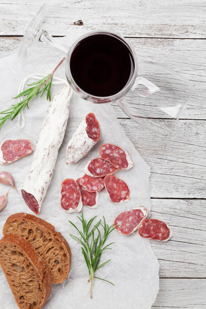 Salami, bread and red wine glass. Meat antipasto platter on wooden table. Top view - Photo, Image