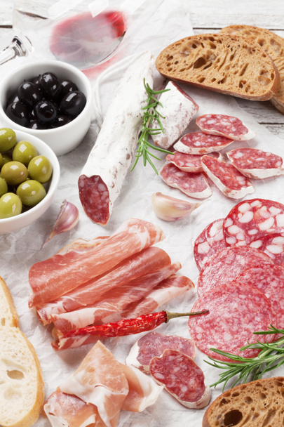 Salami, jambon tranché, saucisse, prosciutto, bacon, pain grillé, olives. Assiette antipasto à la viande et vin rouge sur table en bois
 - Photo, image